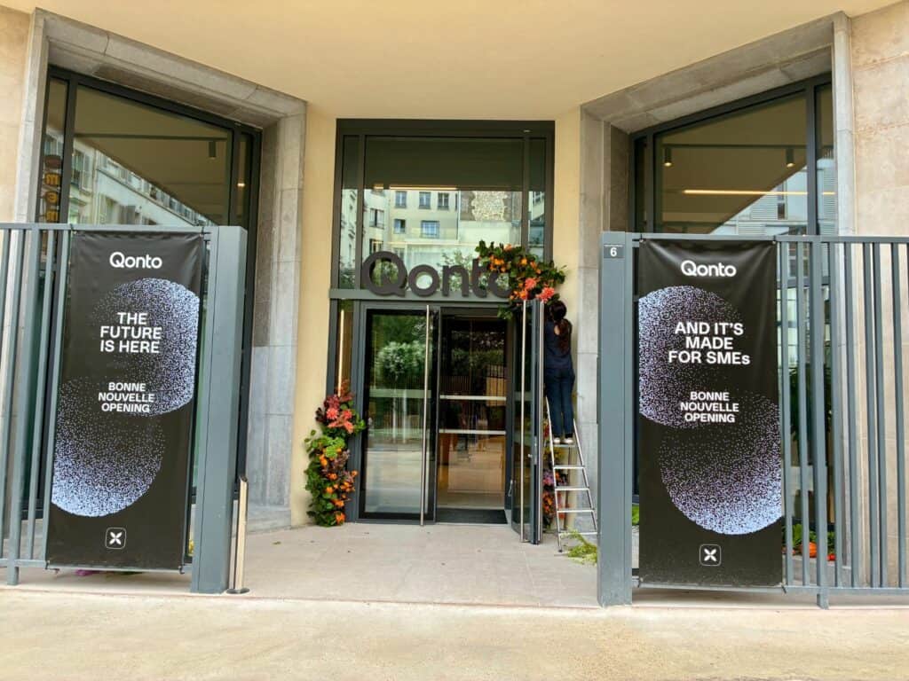 Entrée du siège Qonto avec deux bannières noires « The future is here » et « And it’s made for SMEs », une personne fleurit la porte