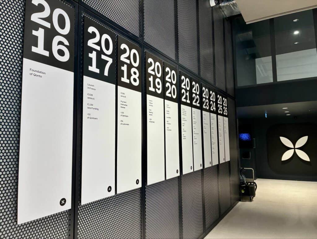 Frise murale des années 2016 à 2026 retraçant les étapes de l’histoire de Qonto, avec le logo en fleur à droite