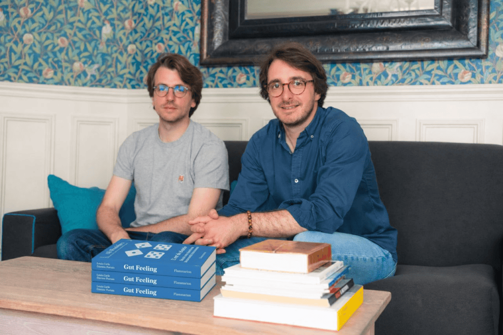 Deux hommes assis sur un canapé devant une table basse où sont empilés plusieurs exemplaires du livre Gut Feeling et d'autres livres